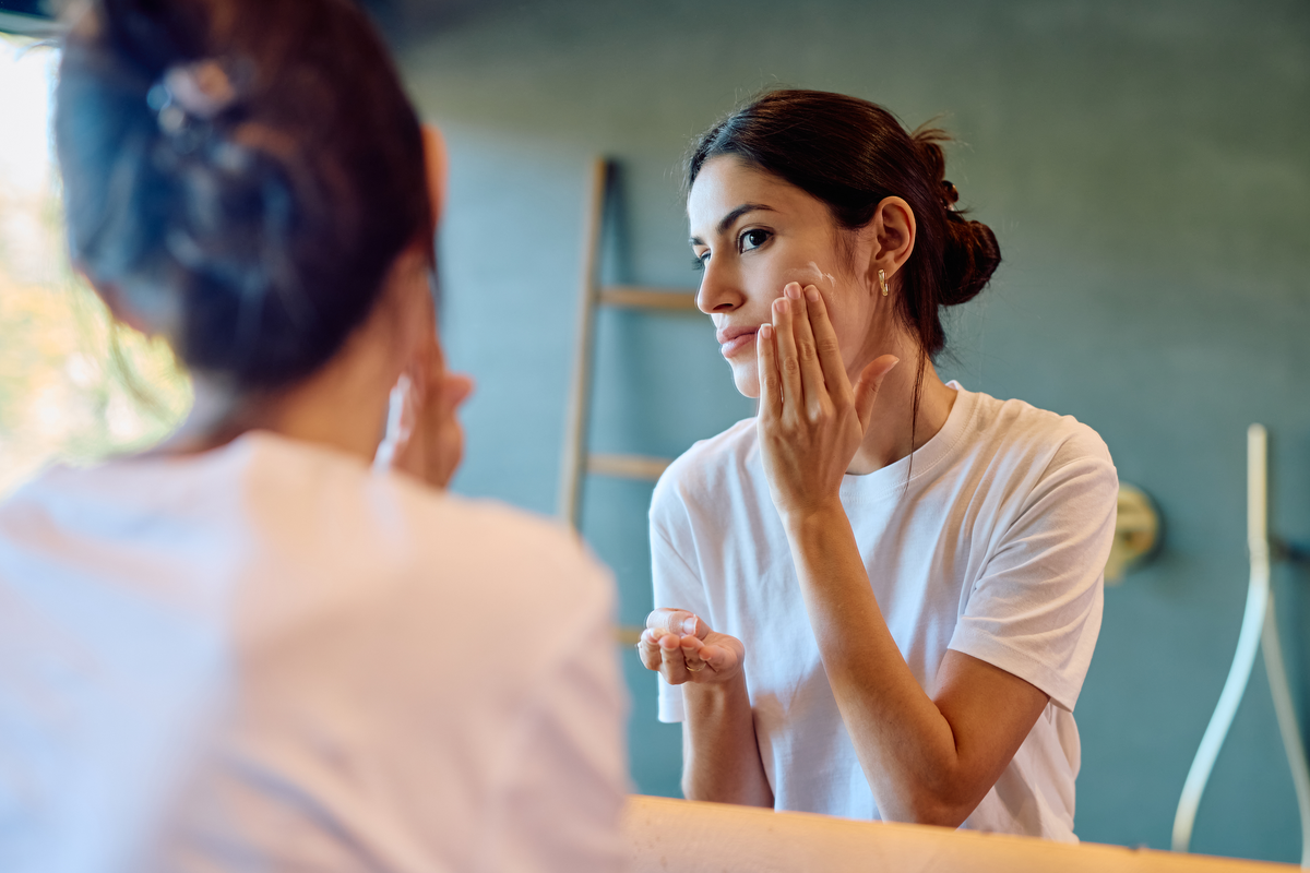 Woman applying moisturizer in a mirror.
